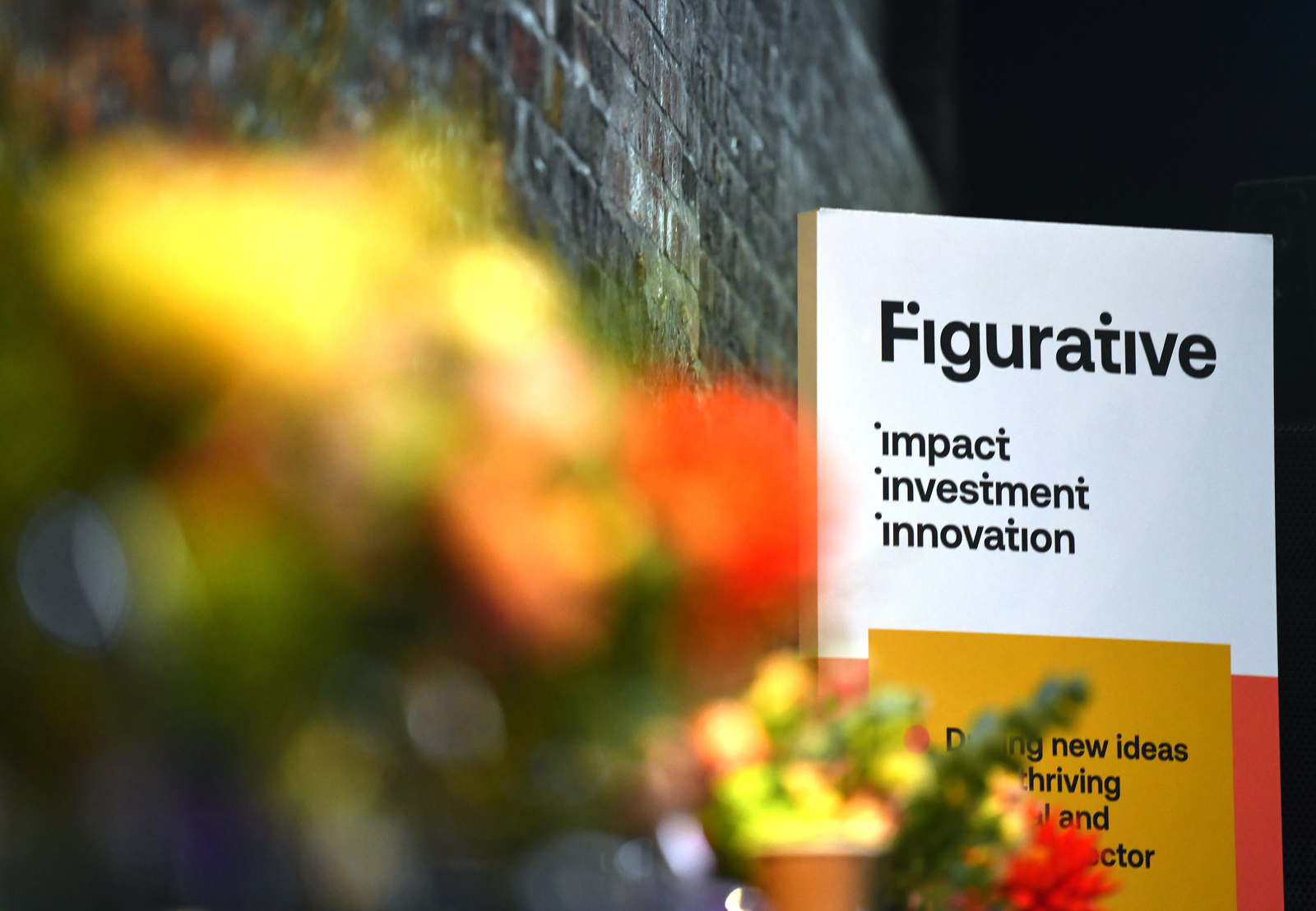 a sign next to a brick wall. The sign reads "Figurative. Impact, Investment, Innovation."