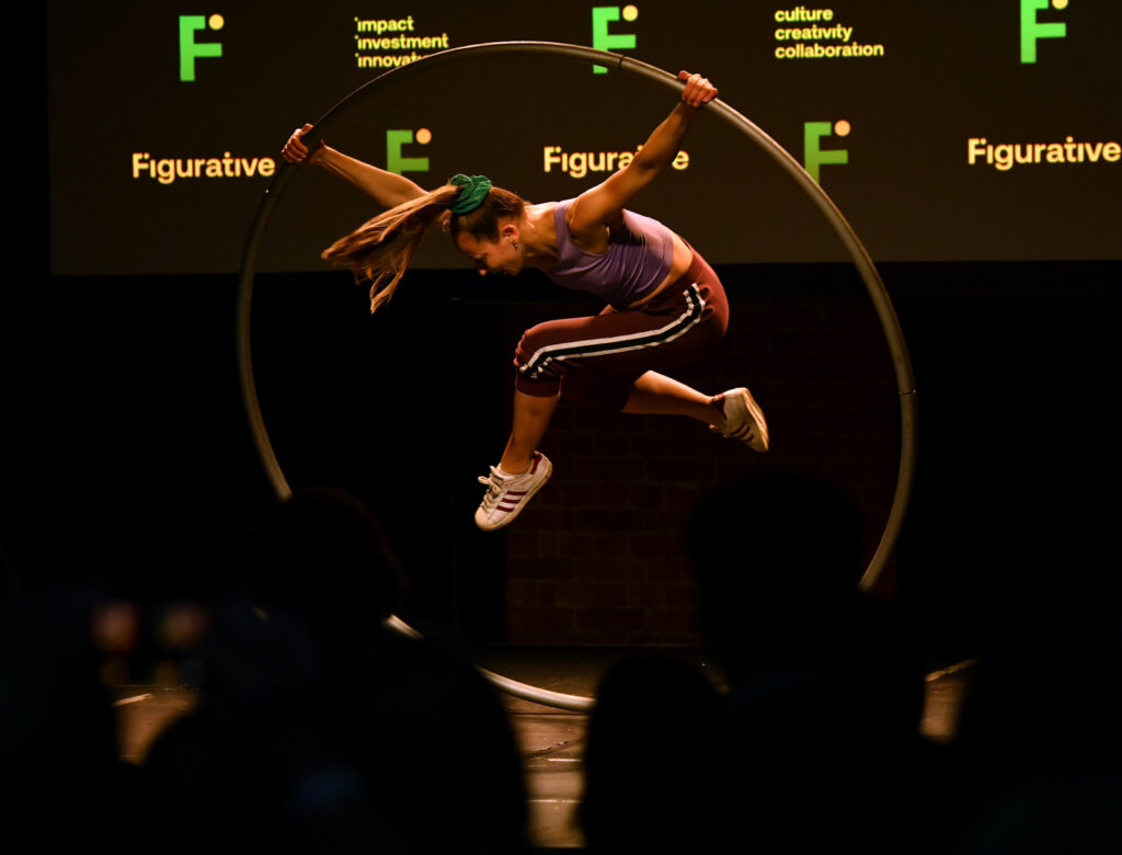 a woman jumping in the air while holding a Cyr wheel, in front of a crowd