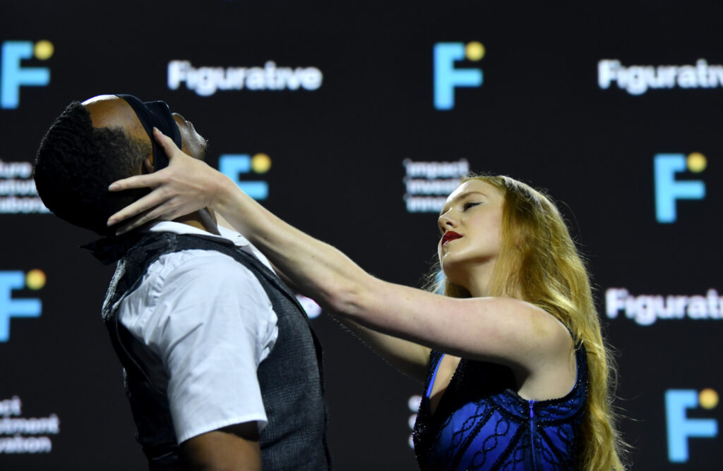 a female dancer reaches out to hold the head of a blindfolded male dancer.