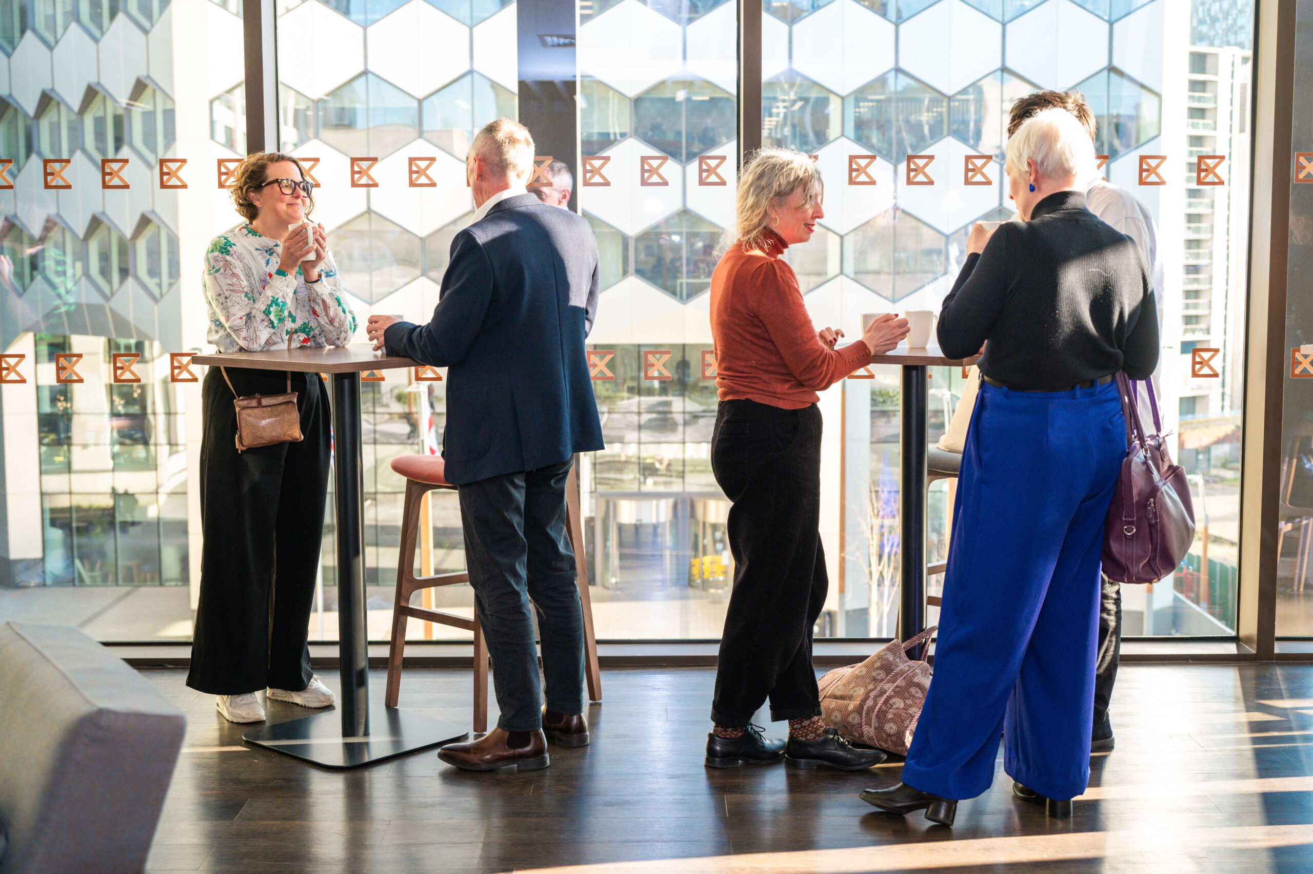 A group of 5 people standing at poser tables before a large window