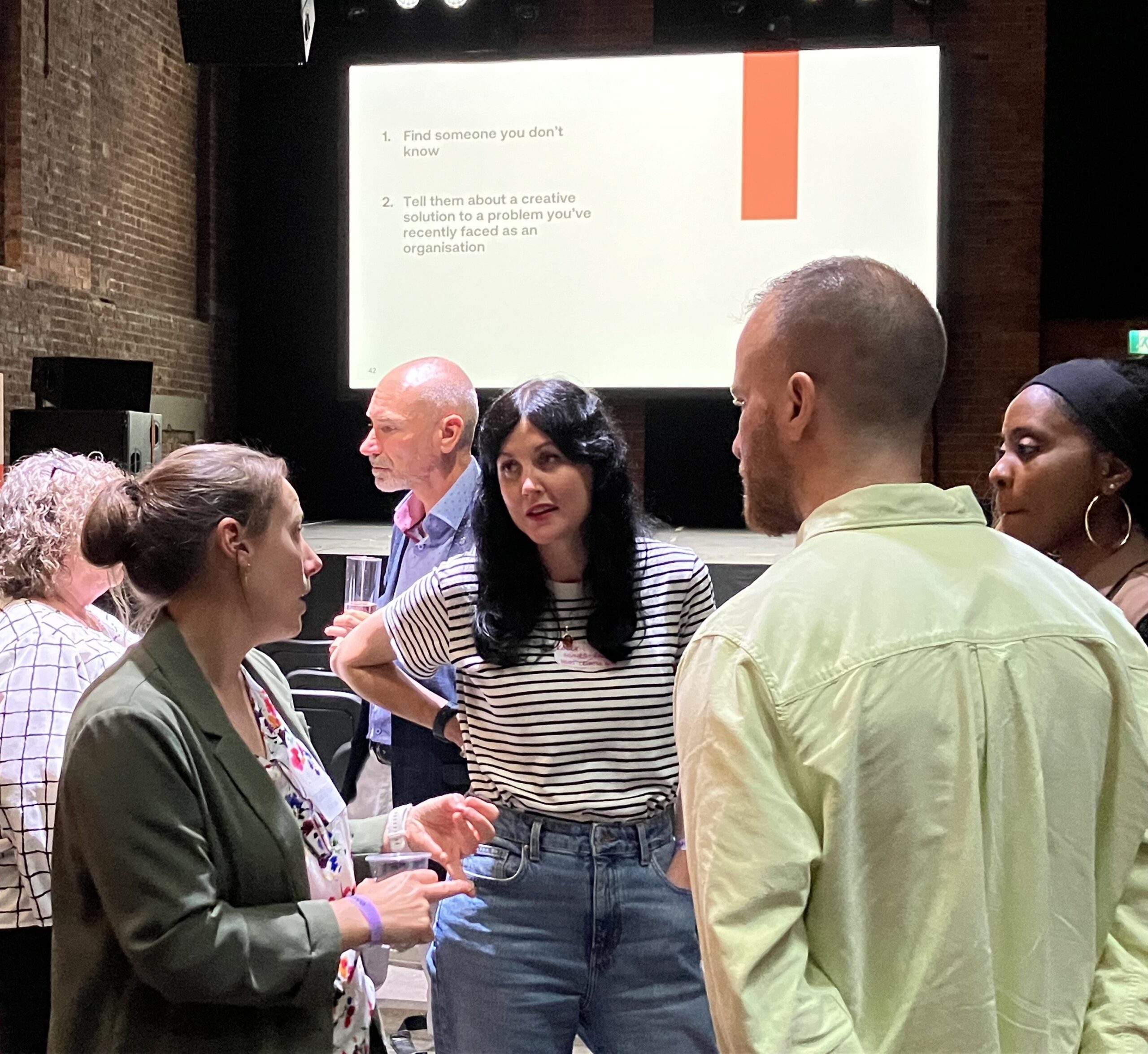 A group of three people standing together talking in front of a presentation on a stage