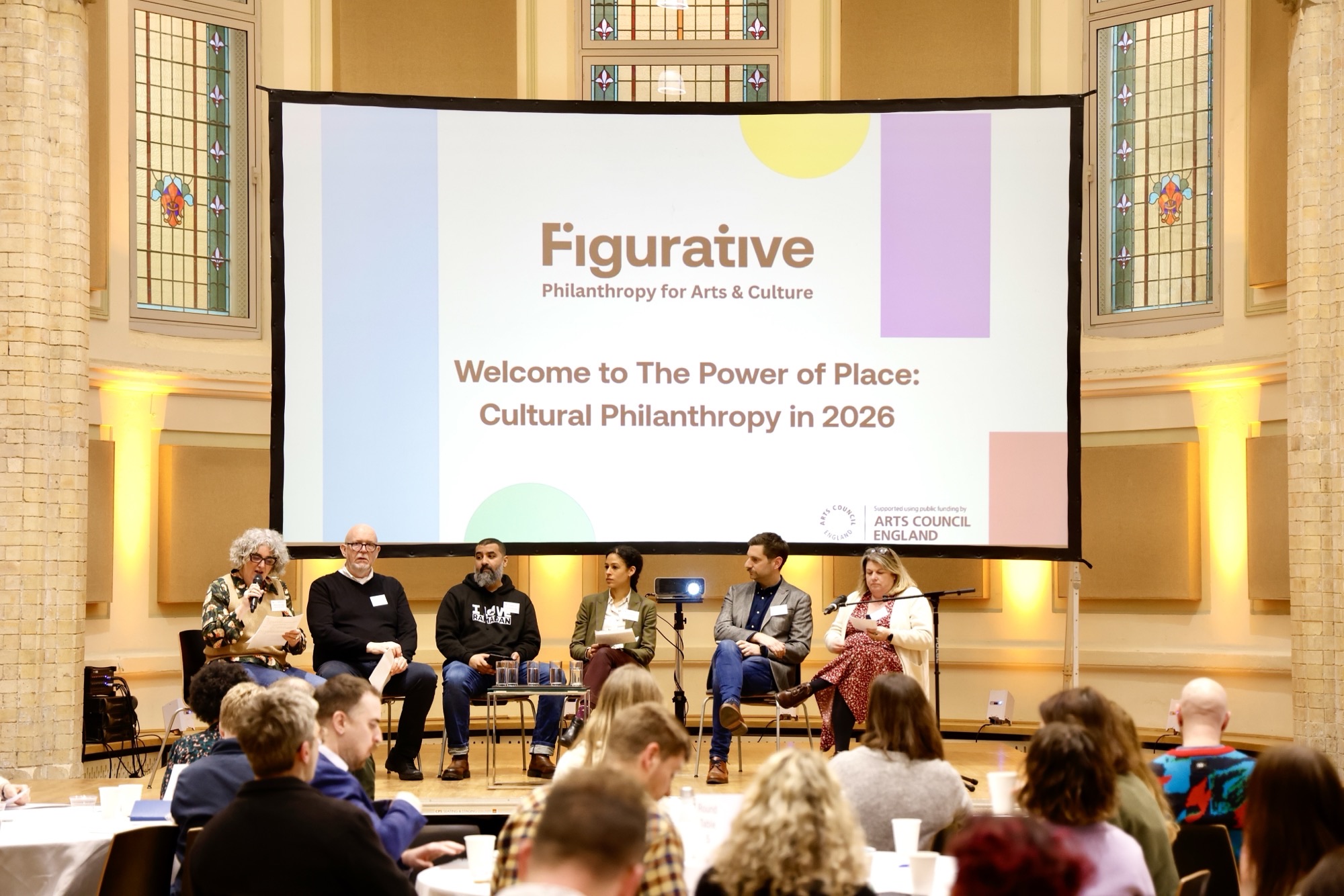 A panel are seated on a stage in front of a large screen with words Welcome to the Power of Place: Cultural Philanthropy in 2026