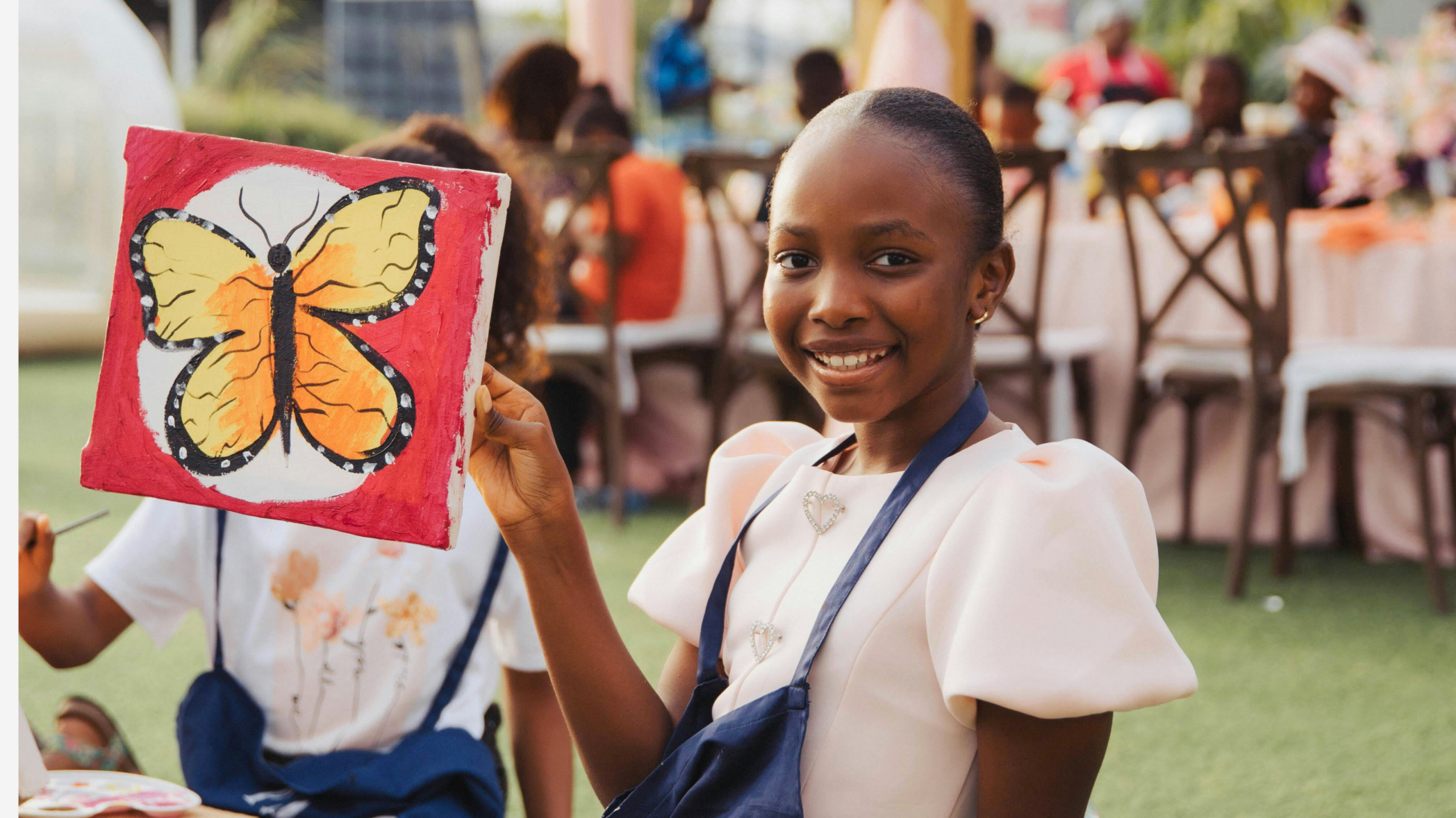 Seated girl smiling holding a painted picture of a butterfly.
