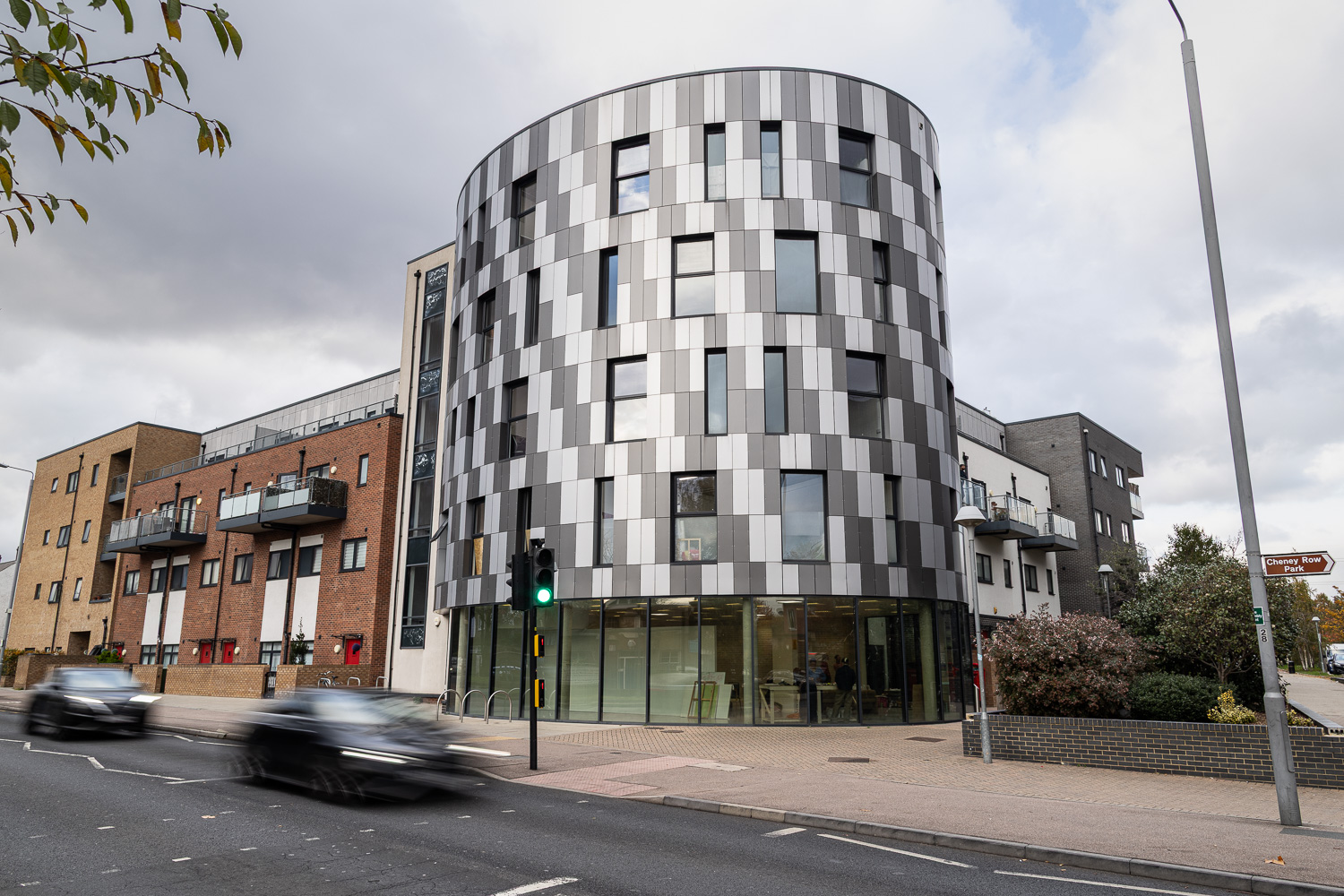 External image of a building with modern curved grey exterior.. Cars are passing and the skies around it are grey