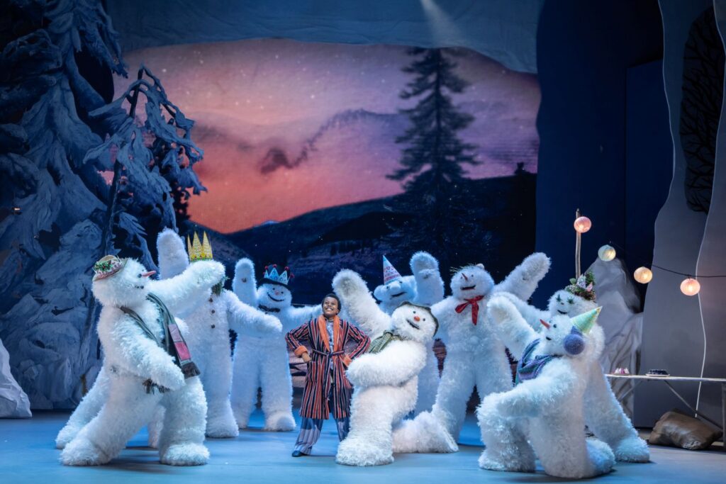 Production image from The Snowman. A group of Snowmen on stage, with The Boy smiling in the centre.